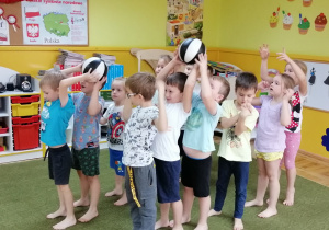 Dzieci pzenoszą w rzędach piłke nad głową
